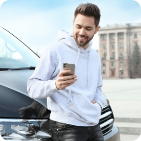 Man leans against vehicle and scrolls his cellphone.